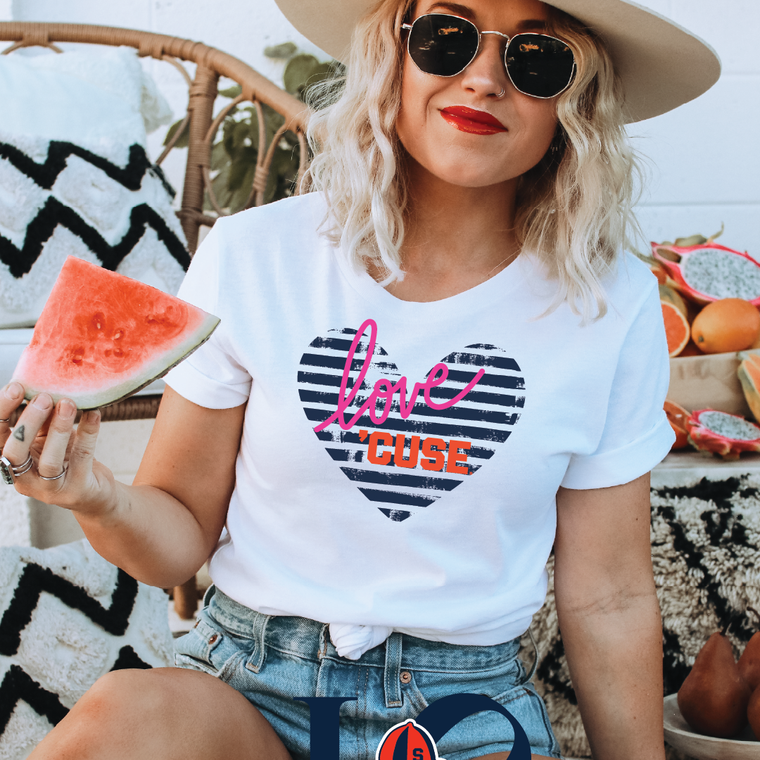Woman wearing white t-shirt with distressed navy striped heart graphic, pink "love" script, and bold orange "’CUSE" lettering — styled with denim shorts and summer hat for casual Syracuse fan look