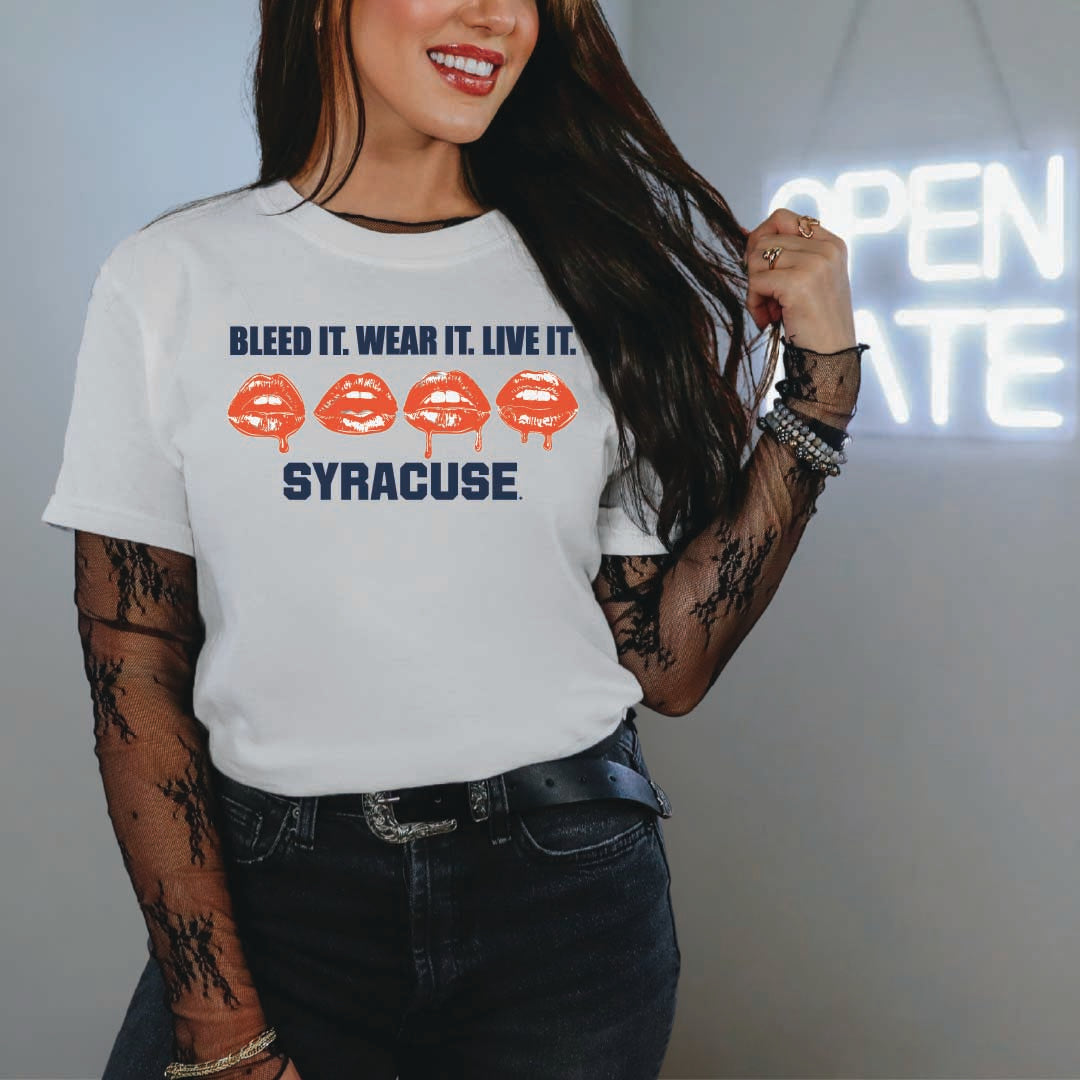 Woman wearing white t-shirt with bold "Bleed It. Wear It. Live It." text, four red kiss prints, and navy "Syracuse" lettering — styled with lace sleeves and edgy accessories for a bold fan look