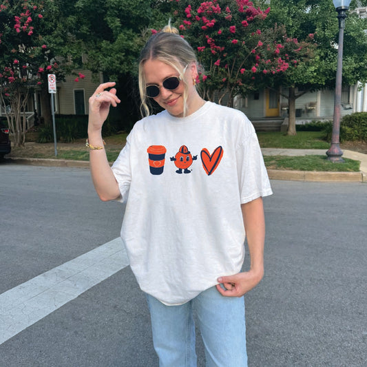 Woman wearing white t-shirt featuring orange coffee cup, Otto the Orange mascot, and heart sketch graphics — styled casually with light denim and gold jewelry


