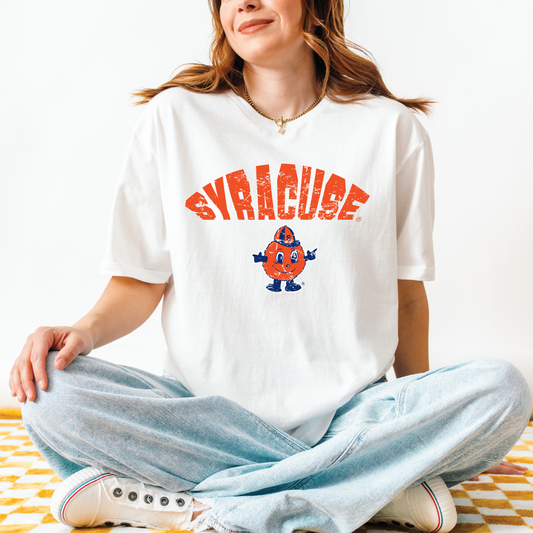 Model wearing white t-shirt with distressed red “SYRACUSE” arch and full-color Otto the Orange mascot – sitting cross-legged on yellow checkered blanket
